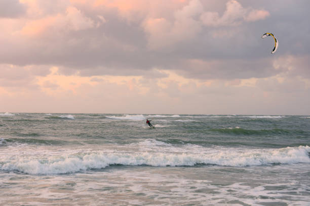 brave man practicing sport called Kitesurfing on a windy day above a rough sea with high waves