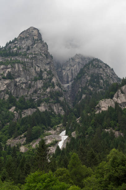 A majestic mountain with a cascading waterfall is surrounded by dense forest and mist creating a stunning and dramatic natural landscape capturing the beauty of the wilderness.