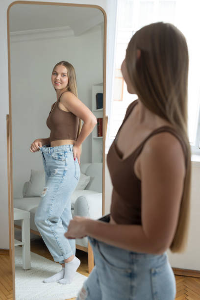 istock Smiling woman trying large jeans and looking at mirror 2175206707