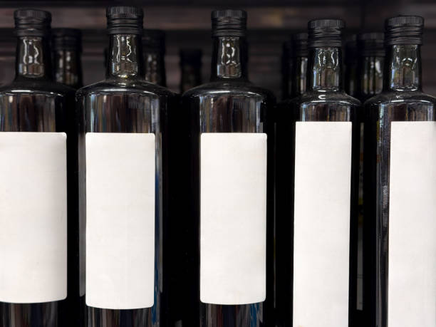 Multiple dark-colored glass bottles with blank white labels neatly lined up on a store shelf, ready for sale.