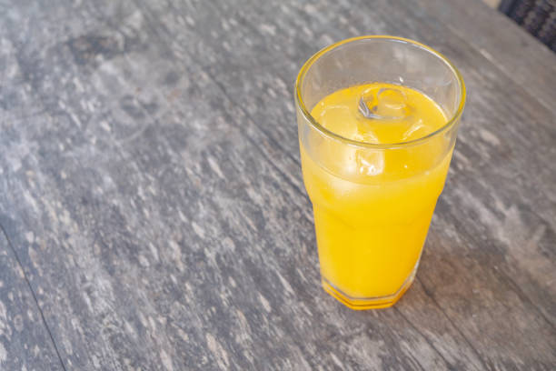 A glass of freshly squeezed orange juice with ice cubes on a wooden table. The bright yellow color of the juice is refreshing.