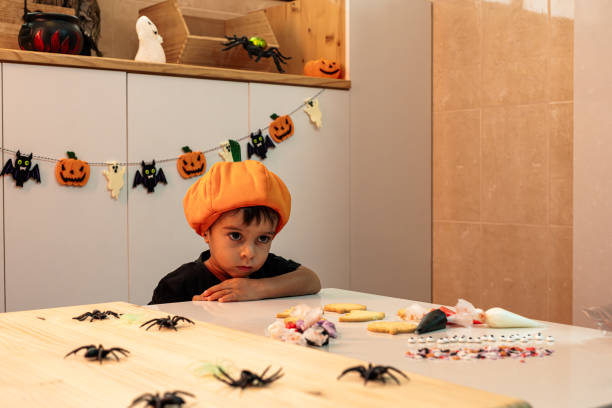 istock A young boy in an orange hat sits at a table with Halloween decorations. 2175266064