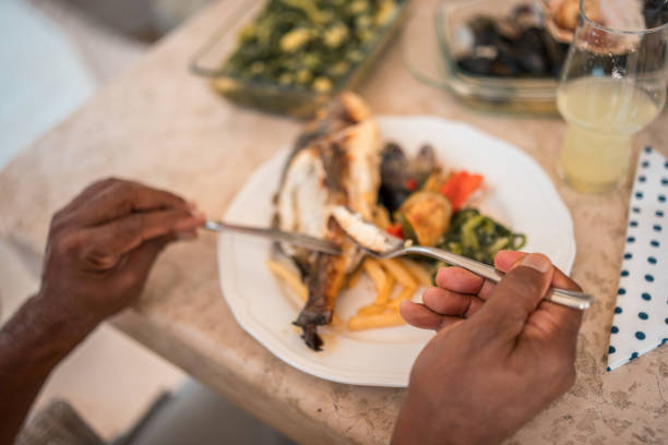 Slice of the pickled atlantic herring impaled on a fork above the same sliced herring with chopped green onion seasoned with cooking oil, close-up in selective focus