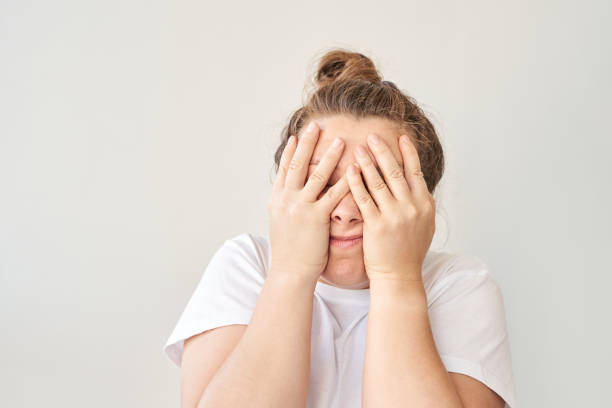 istock Woman covering face with hands in shirt against plain background expressing 2175299418