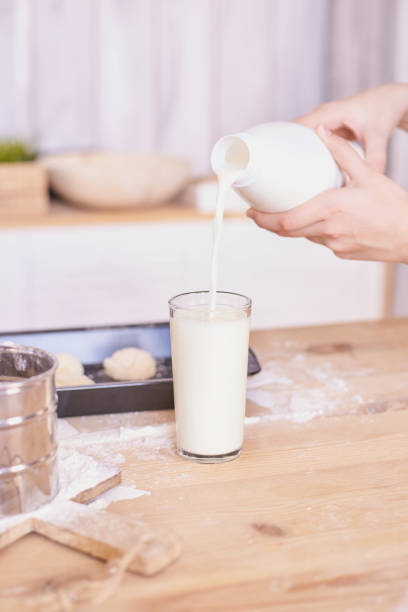 istock Pouring fresh milk into glass on a wooden kitchen table with baking ingredients 2175300362