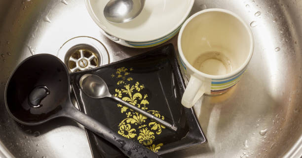 Dirty dishes in kitchen sink, including mug, bowls, spoons, and black plate with yellow patterns. stock photo