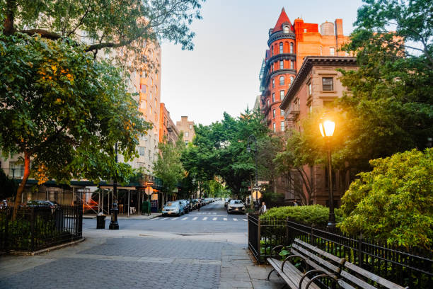 This is a photograph of a Brooklyn Height’s park bench with an illuminated street light and residential buildings in the background in summer.