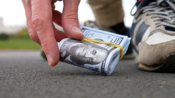 istock Close-up of a man picking up a stack of hundred dollar bills from the ground 2175307701