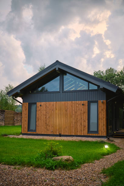 istock Modern wooden cabin surrounded by greenery under a cloudy sky in the late afternoon sunlight 2175307876