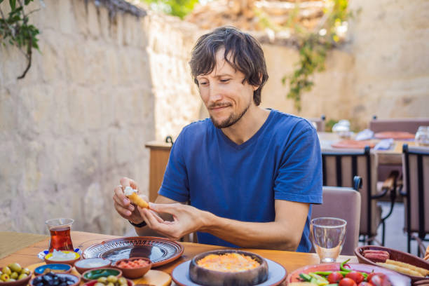 istock Man eating turkish breakfast. Turkish breakfast table. Pastries, vegetables, greens, olives, cheeses, fried eggs, spices, jams, honey, tea in copper pot and tulip glasses, wide composition 2175309577