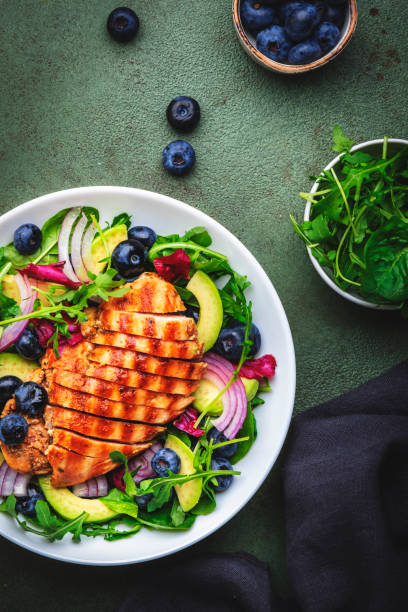 istock Green salad with grilled chicken, avocado and blueberries, rustic background, top view 2175323697