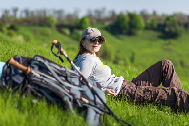 Resting woman hiker sitting enjoying the sun during hiking travel trek. Beautiful young female hiker with backpack.