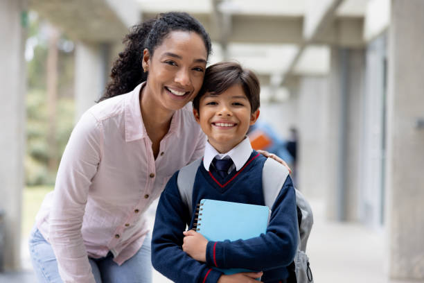 Portrait of a happy Latin American teacher smiling with a young student at the school and looking at the camera