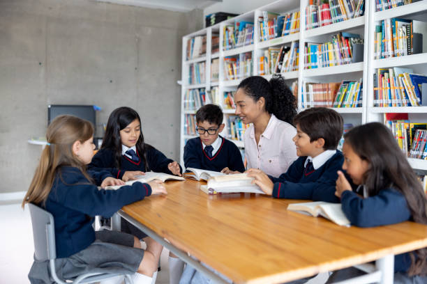 istock Teacher with a group of elementary students reading books at the library 2175339415