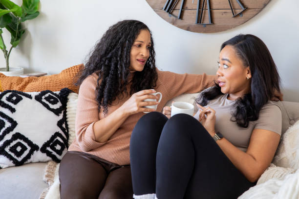 istock Two women, seated on a couch, enjoy a coffee break and chat together. 2175345756