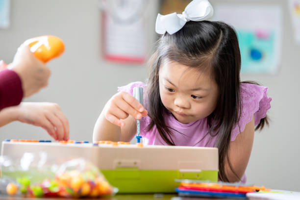 istock Little girl with Down Syndrome concentrates while using STEM educational building toy in special education classroom 2175352719