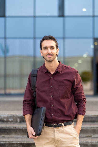 istock Young professional holding a laptop case while standing outside a corporate building 2175357119