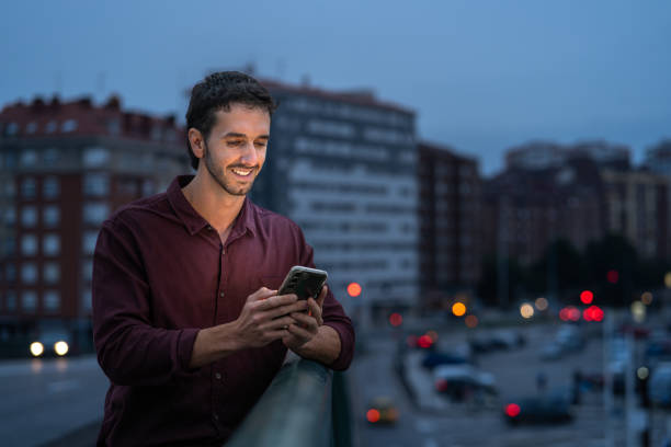 istock Smiling young man on a city bridge at dusk, using a smartphone 2175357175