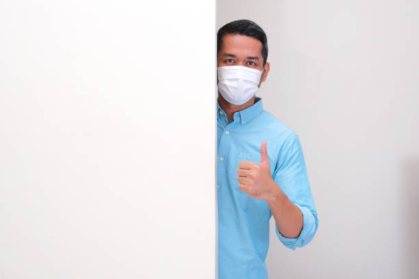 istock A man wearing medical face mask peeking from behind wall and give thumbs up 2175361601