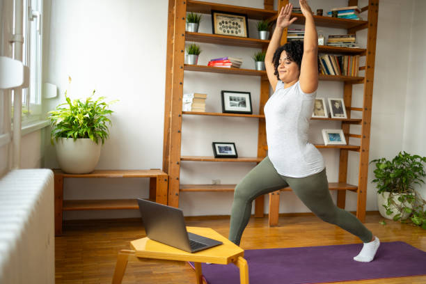 istock Happy woman practicing warrior pose during online classes on laptop in yoga room 2175376104