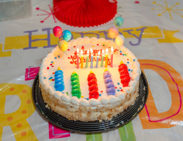 Birthday cake with a candle in the middle with young people around the table.
