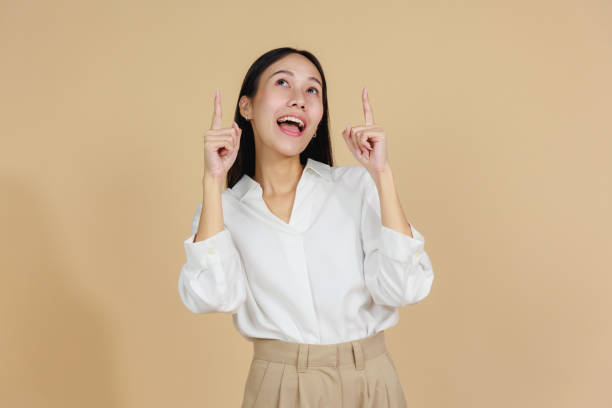 istock Smiling Woman Pointing Upwards with Enthusiasm, Beige Background 2175383497