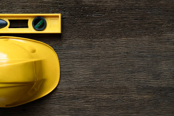 Yellow building level and helmets on the old wood table, engineering eqipment tool concept, top view.