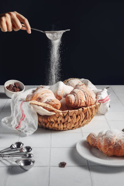 French breakfast, pastries for coffee. close-up wicker basket with fluffy freshly baked croissants. A woman's hand sprinkles croissants with powdered sugar. Front view.