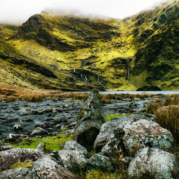 A tranquil valley featuring vibrant green slopes and multiple waterfalls flowing down rocky terrain. Early morning mist adds to the peaceful atmosphere of this natural landscape.