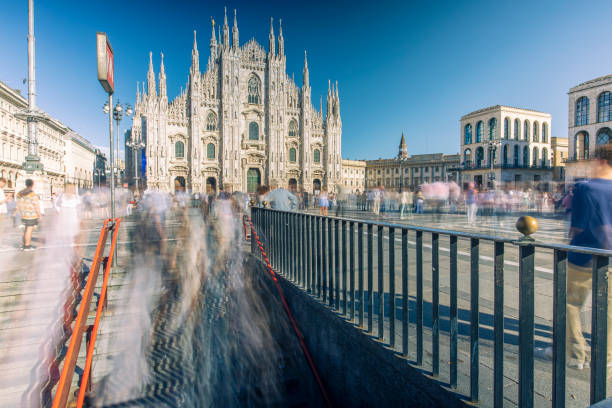 Milan, Italy - September 28, 2024: long exposure shot of Piazza del Duomo, people are motion blurred while coming out of a subway station under a clear blue sky.