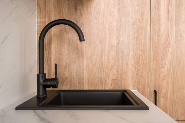istock Modern black kitchen sink with a sleek faucet on a white countertop surrounded by wood cabinetry 2175431594