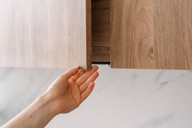istock Hand reaching for a wooden cabinet door in a modern kitchen during daylight 2175431607