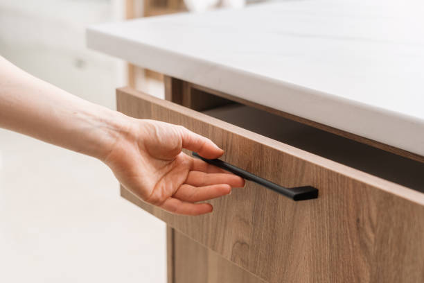 Hand reaching to open a wooden drawer with a black handle in a modern kitchen