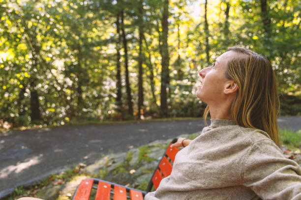 A woman leans back on a red park bench, enjoying the peaceful atmosphere of a forest. Sunlight filters through the trees on a quiet path.
