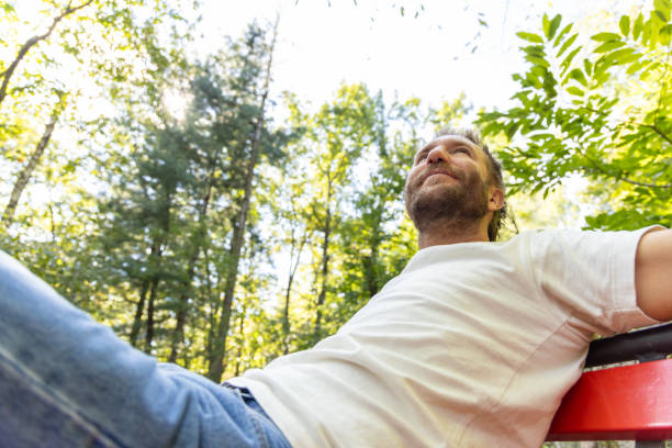 istock Man Relaxing on a Park Bench in Sunlit Forest 2175438513