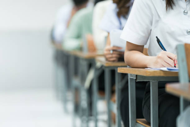 istock Students Taking Exam in Classroom Setting. Students in uniforms are seated in a classroom, writing answers during an exam, highlighting focus and academic testing. 2175454420