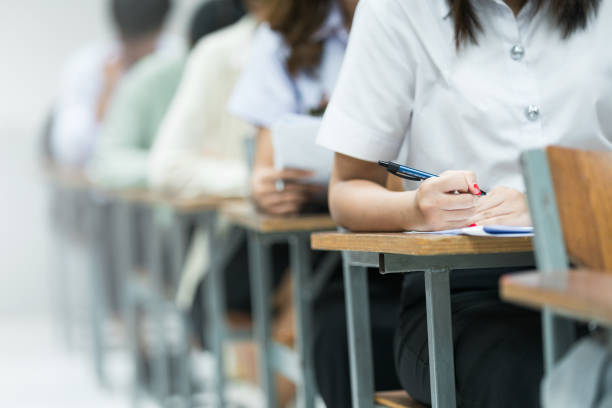 istock Students Taking Exam in Classroom Setting. Students in uniforms are seated in a classroom, writing answers during an exam, highlighting focus and academic testing. 2175454422