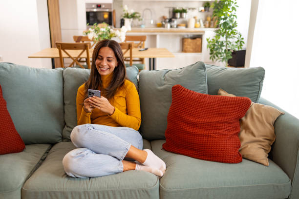 Woman Relaxing At Home Using Smartphone On Couch