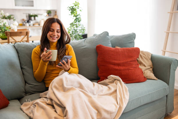 istock Smiling Woman Relaxing on Couch with Coffee and Smartphone 2175459676