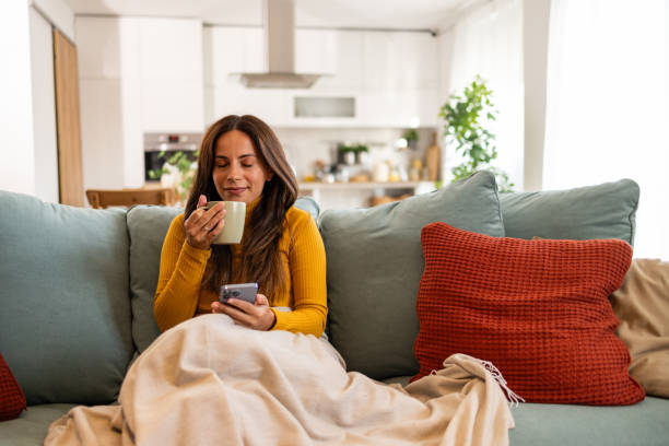 istock Smiling Woman Relaxing on Couch with Coffee and Smartphone 2175459714