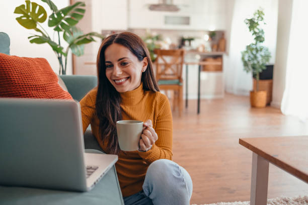 istock Smiling Woman Holding Coffee Cup While Using Laptop at Home 2175460057