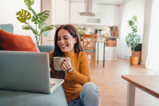 istock Smiling Woman Holding Coffee Cup While Using Laptop at Home 2175460089