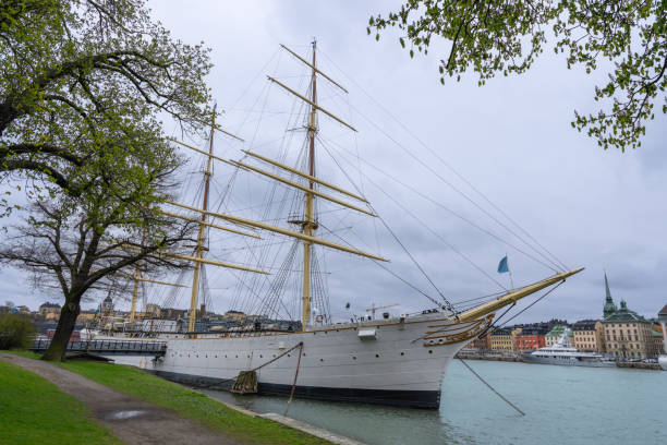 A majestic white sailing ship docks in Stockholm harbor with the city skyline in the background. Stockholm, Sweden.