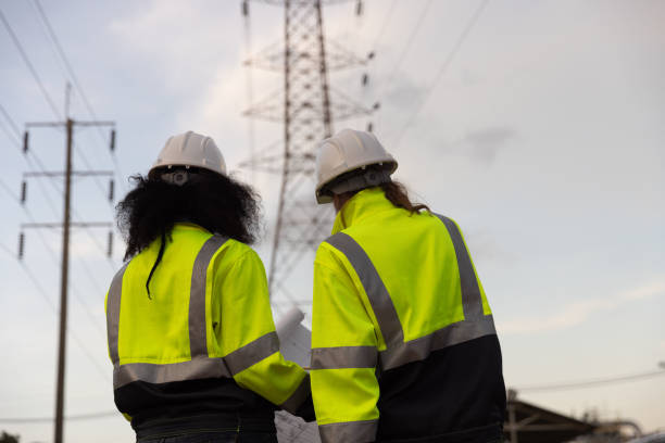 istock Back view of two female industry engineers working and discussing in front of a voltage-generating station and  high voltage pole 2175487837
