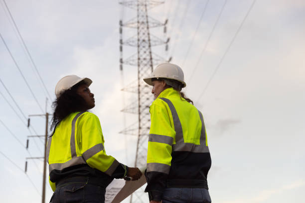 istock Back view of two female industry engineers working and discussing in front of a voltage-generating station and  high voltage pole 2175487842