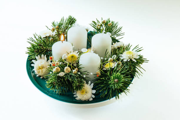 four white advent candles, wreath decoration with flowers and pine, isolated, first advent candle lit