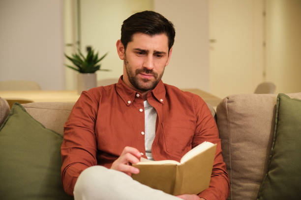 istock Focused young man reading a book on the couch at home 2175492992