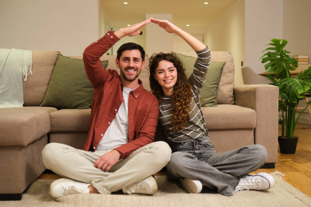 istock Happy couple making a roof shape with their arms while sitting on the floor 2175493685