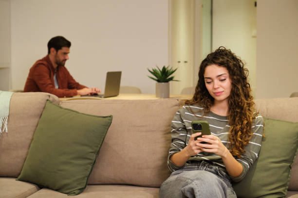 istock Young woman using smartphone while boyfriend is working on laptop in background 2175493927