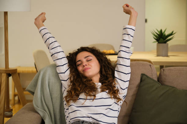 istock Young woman stretching arms while relaxing on sofa at home 2175496073